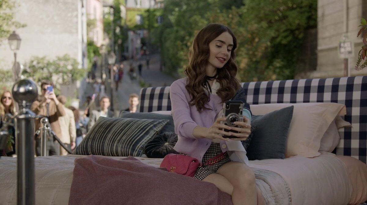 エミリー、パリへ行くのワンシーン。紫色のジャケットとベッドの上に紫色のブランケット