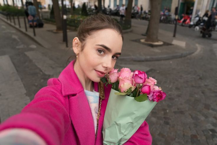 「エミリー、パリへ行く」の中に出てくるワンシーン。エミリーがショッキングピンクのコートを着て、ピンク色の花束を持っている