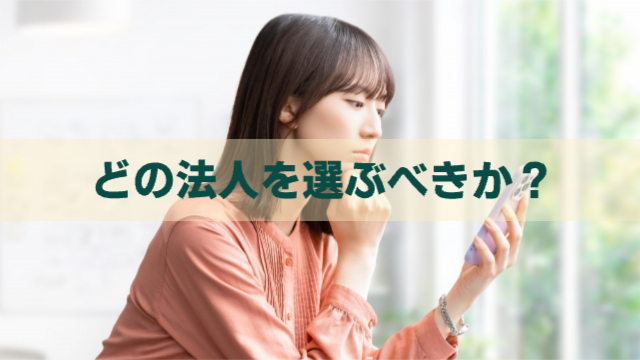 女性がスマホを見ながら考えている様子「どの法人を選ぶべきか？」