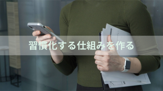 女性が資料を片手に持ってもう片手でスマホを触っている様子「習慣化する仕組みを作る」